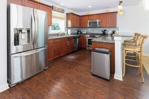 A kitchen with stainless steel appliances, wooden cabinets, and a granite countertop. - Dog Friendly Gorgeous Corolla Home Pool & Hot Tub (Corolla)