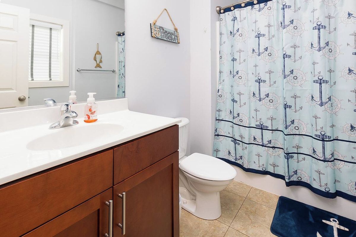 A bathroom with a white sink, wooden cabinets, a toilet, and a shower curtain with an anchor pattern.