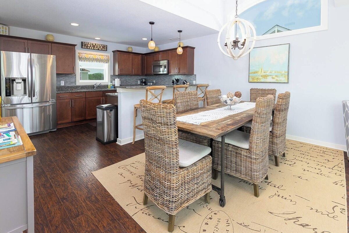 A modern kitchen with stainless steel appliances, a dining area with wicker chairs, and a view of the outdoors.