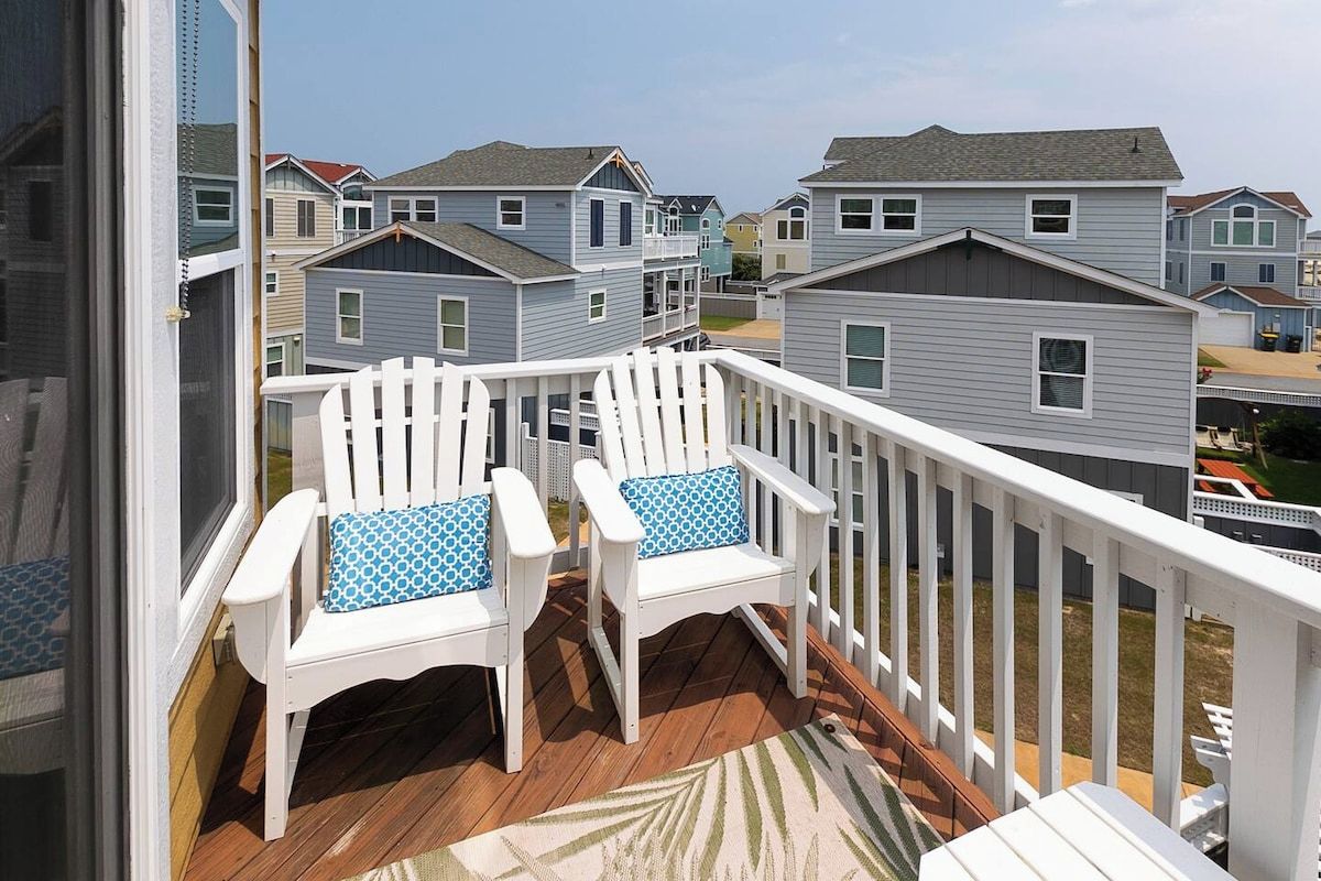 Un balcon agrémenté de deux fauteuils Adirondack blancs et d’un tapis à motifs.