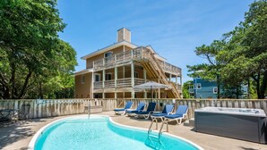 A swimming pool with lounge chairs and a hot tub, surrounded by a wooden deck and trees.