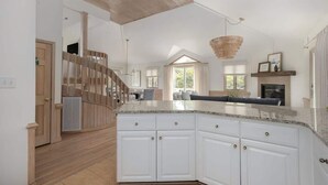 A spacious kitchen with white cabinets, a large island, and a wooden staircase.