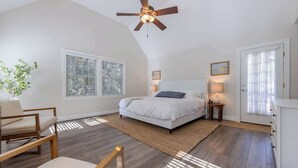 A bedroom with a bed, a ceiling fan, a window, a plant, and a door.