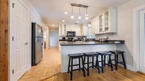 A modern kitchen with white cabinets, a central island with bar stools, and a built-in microwave.