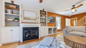 A cozy living room with a fireplace, wooden shelves, a sofa, and a staircase.