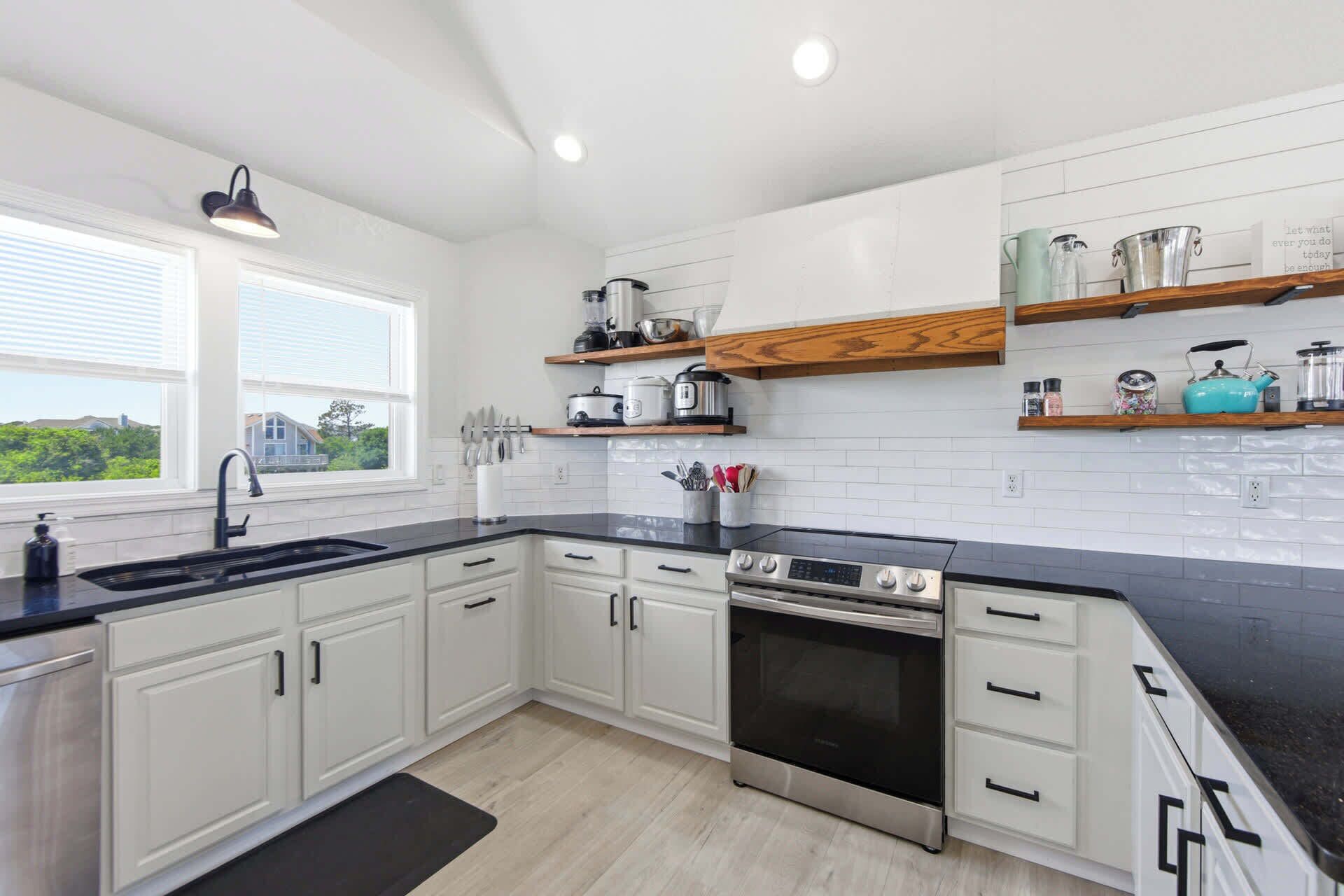 A modern kitchen with white cabinets, black countertops, a stainless steel oven, and wooden shelves above the counter.