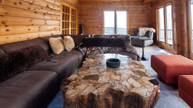 Ein gemütliches Blockhaus-Interieur mit einem Stehtisch, einer braunen Ledersofa und einem roten Hocker.