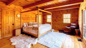 Ein Schlafzimmer einer Holzhütte mit einem Himmelbett, einem Fellteppich und einem Fenster mit Blick auf Bäume.