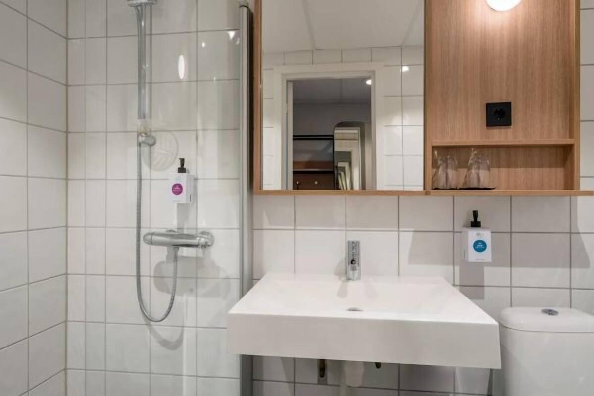 A modern bathroom with a white sink, a glass shower enclosure, and a wooden shelf above the sink.