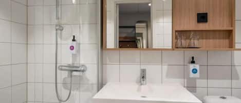A modern bathroom with a white sink, a glass shower enclosure, and a wooden shelf above the sink.