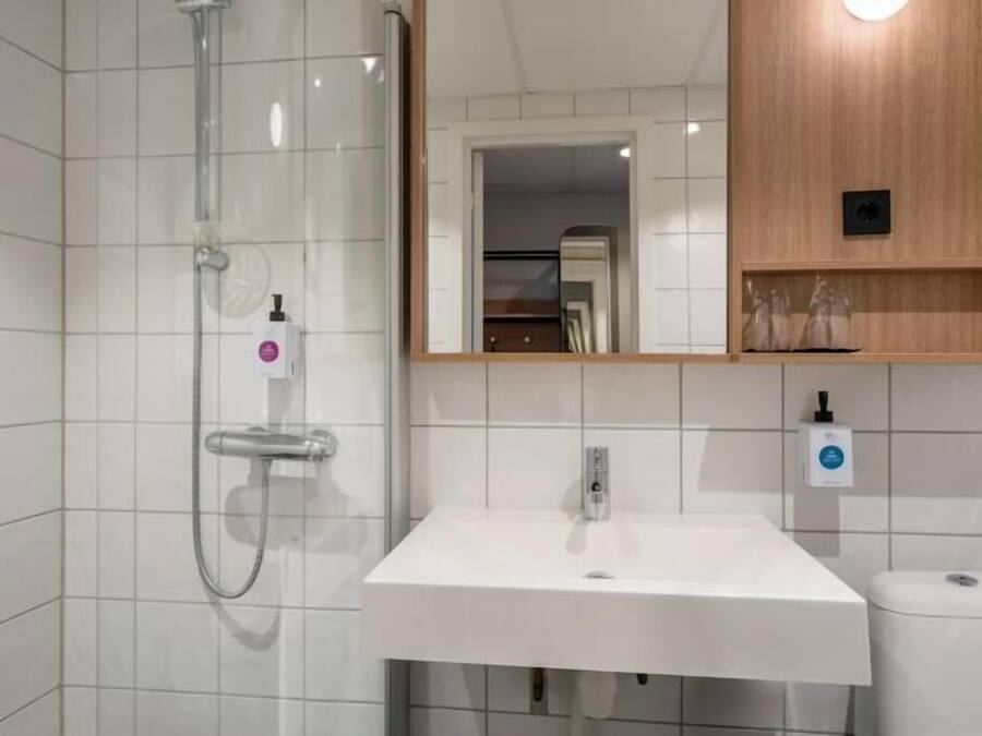 A modern bathroom with a white sink, a glass shower enclosure, and a wooden shelf above the sink.