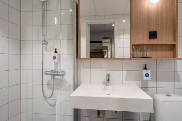 A modern bathroom with a white sink, a glass shower enclosure, and a wooden shelf above the sink. - Quality Hotel Strand Gjøvik (Gjovik)