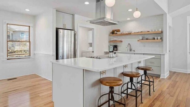 Une cuisine moderne dotée d’un grand îlot central, de tabourets de bar, d’un réfrigérateur en acier inoxydable et d’étagères en bois.
