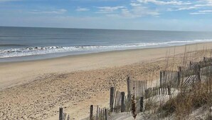 Une plage avec une clôture en bois au premier plan et l’océan en arrière-plan.