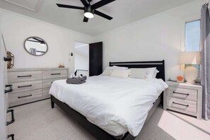 A bedroom with a bed, a nightstand, a mirror, a ceiling fan, and a window with curtains. - Saltwater Pool | Hot Tub | Town of Duck (Duck)