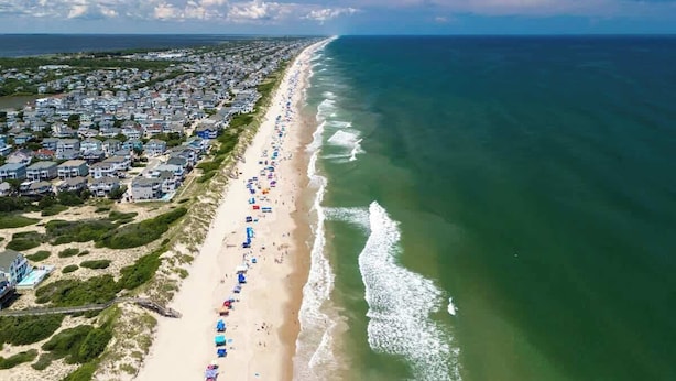An aerial view of a coastal town with a long beach lined with houses and beach umbrellas.