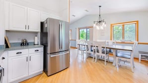 A modern kitchen with white cabinetry, a stainless steel refrigerator, and a dining area with a wooden table and chairs.