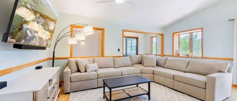 A living room with a sectional sofa, a coffee table, a TV mounted on the wall, and a ceiling fan.