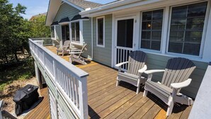 A wooden deck with Adirondack chairs, a covered area, and a house with large windows.