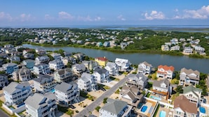 A residential area with houses along a river, featuring a mix of single and multi-story buildings, some with visible balconies and driveways.