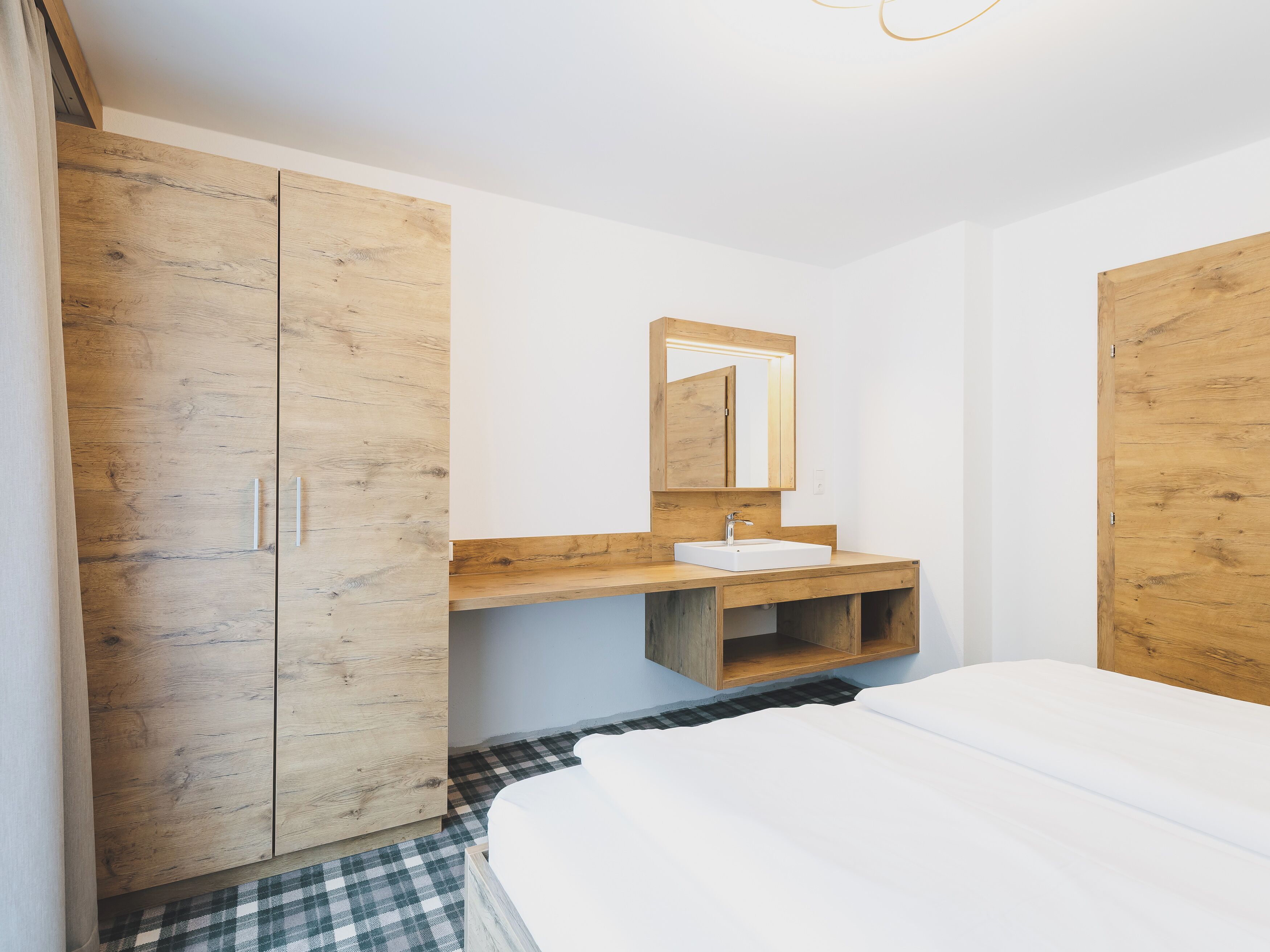 A bedroom with a wooden wardrobe, a bedside table, a mirror, and a bed.