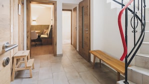 A hallway with a wooden bench, a small stool, and a staircase with a red railing. - Chalet Carina by we rent (Zell am See)