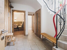 Un pasillo con un banco de madera, un taburete pequeño y una escalera con barandilla roja.
