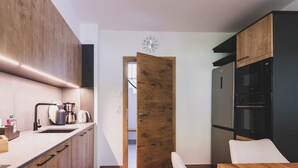 A modern kitchen with wooden cabinets, a built-in oven, and a dining area with a wooden table and bench. - Chalet Carina by we rent (Zell am See)