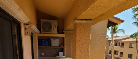 Un balcón con mobiliario de madera, una pequeña cocina y vistas de los edificios circundantes.