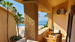 Un patio iluminado por el sol con una mesa y sillas de madera, un carrito pequeño y vistas a la playa y al océano.
