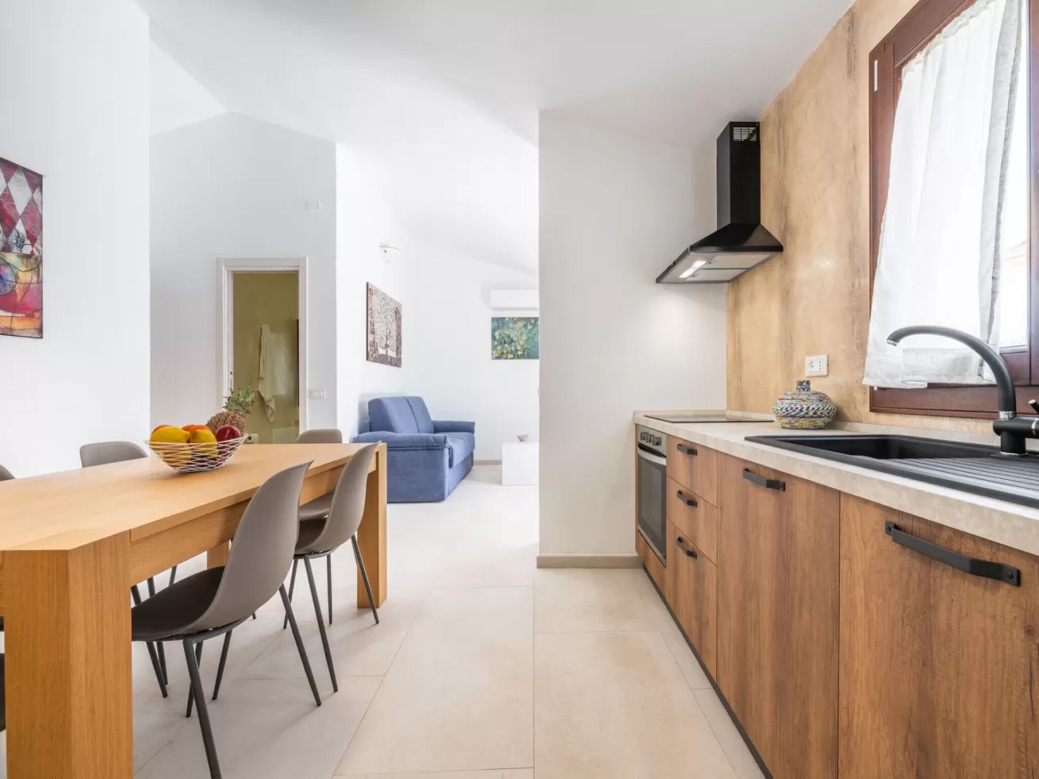A modern kitchen with wooden cabinets, a black range hood, and a window with a curtain.