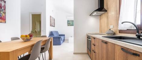 A modern kitchen with wooden cabinets, a black range hood, and a window with a curtain.