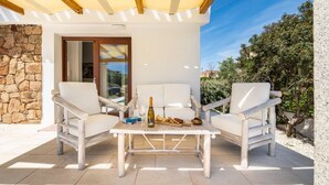 A patio with white furniture, a table with a bottle and glasses, and a stone wall. - Elegant Villa With Private Pool in San Teodoro (San Teodoro)