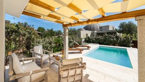 A poolside area with wooden chairs and a table, a pool, and a modern house in the background. - Elegant Villa With Private Pool in San Teodoro (San Teodoro)