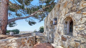 A stone building with a stone pathway leading to a seating area and a fire pit. - Casa Grotto, 1 Bed Stone Cave Cottage, Panoramic Ocean View, Stone Shower, & Gym (San Marcos)