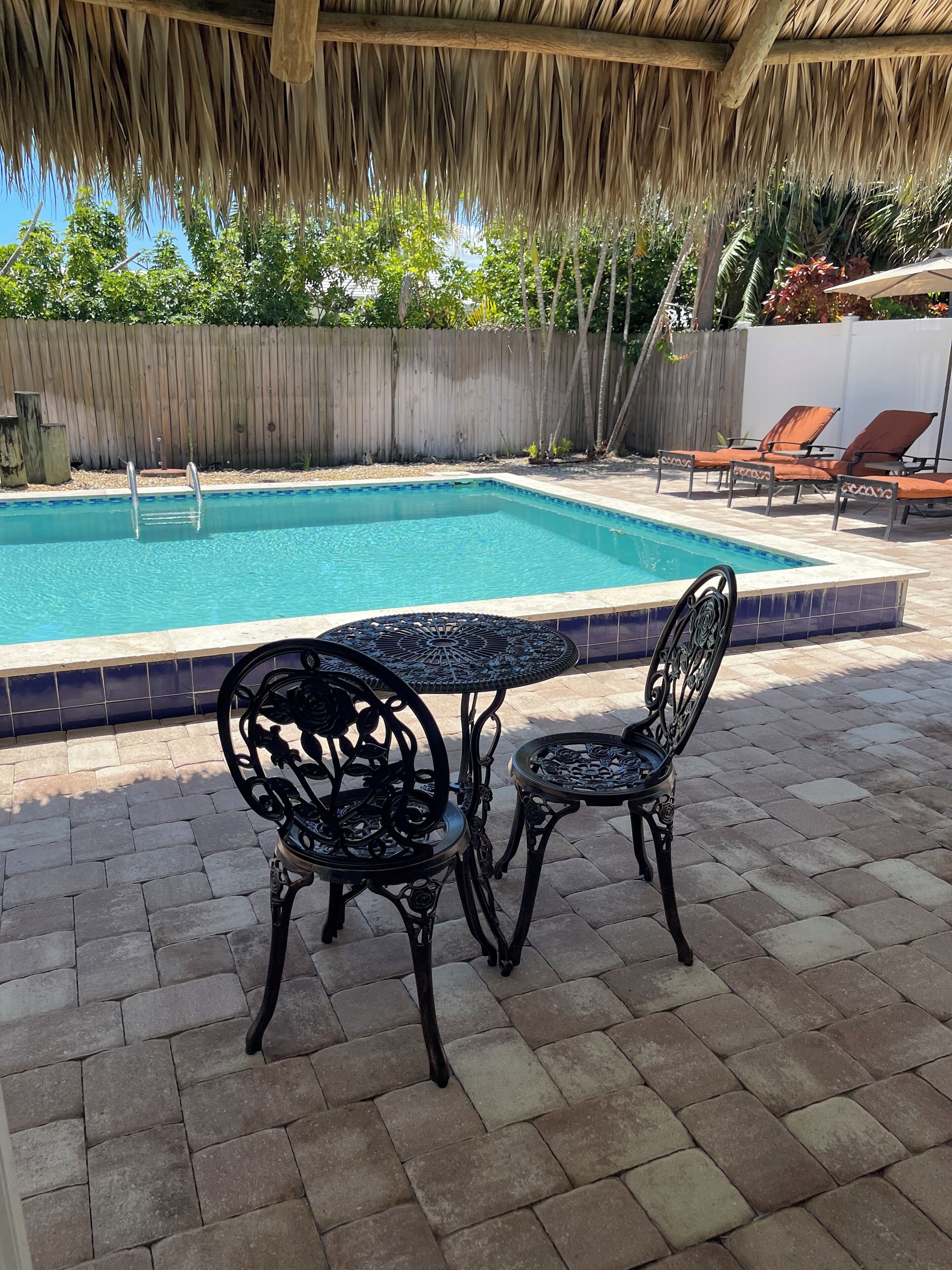 Piscina com deck de madeira, duas cadeiras de metal e uma mesa.