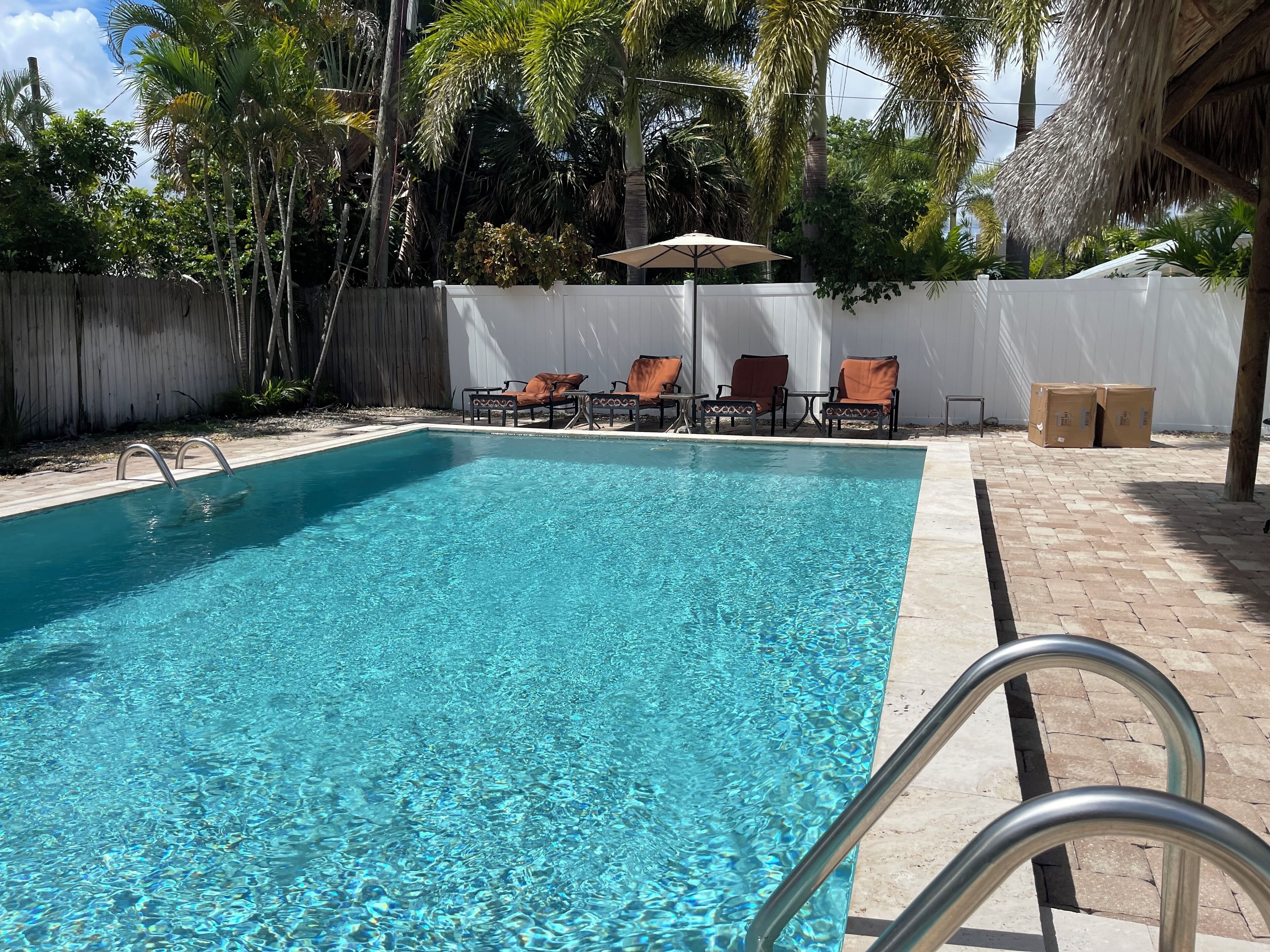 A clear swimming pool with metal railings, surrounded by a white fence and palm trees.