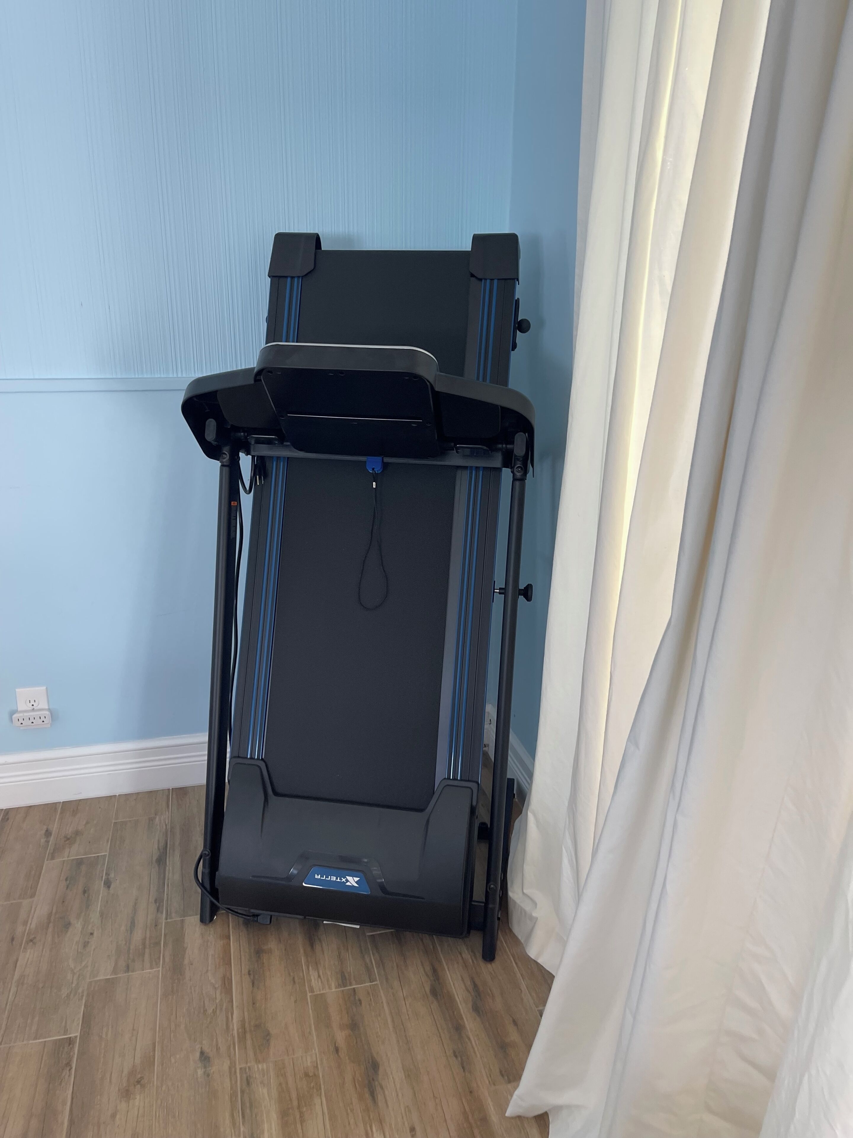 A compact, foldable exercise machine in a room with light blue walls and wooden flooring.