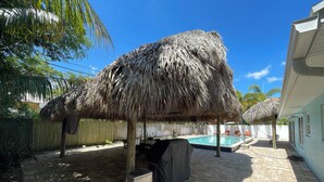 A backyard with a pool, a covered grill, and a thatched umbrella.