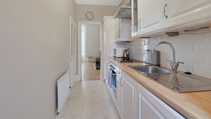 A narrow kitchen with white cabinets, a stainless steel sink, and a wooden countertop. - Heaton House Apartment - North East Escapes (Tynemouth)