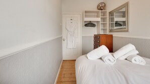 A bedroom with a bed, a wooden dresser, a white robe, a mirror, and a fan. - Heaton House Apartment - North East Escapes (Tynemouth)