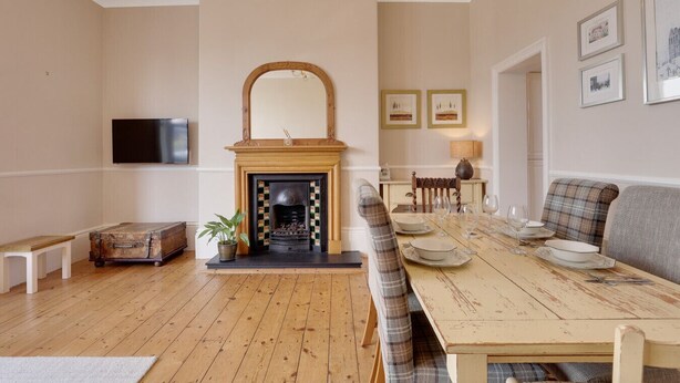 A living room with a fireplace, a television mounted on the wall, a dining table with chairs, and a sofa. - Heaton House Apartment - North East Escapes (Tynemouth)