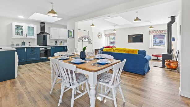 A modern kitchen with white cabinets, a dining table set for four, and a blue sofa in the living area.