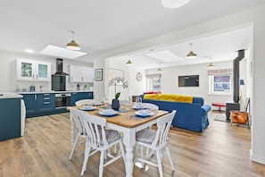 Een moderne keuken met witte kasten, een eettafel voor vier personen en een blauwe bank in de woonkamer.
