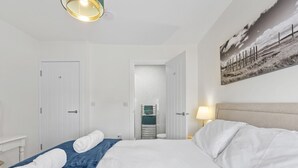 A hotel room with a bed, a desk, a lamp, and a painting on the wall.