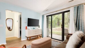 A modern living room with a white TV stand, a brown sofa, and a large sliding glass door leading to a deck.