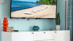 A modern living room with a flat-screen TV mounted on a light blue wall, a white cabinet with wooden legs, and a small potted plant.