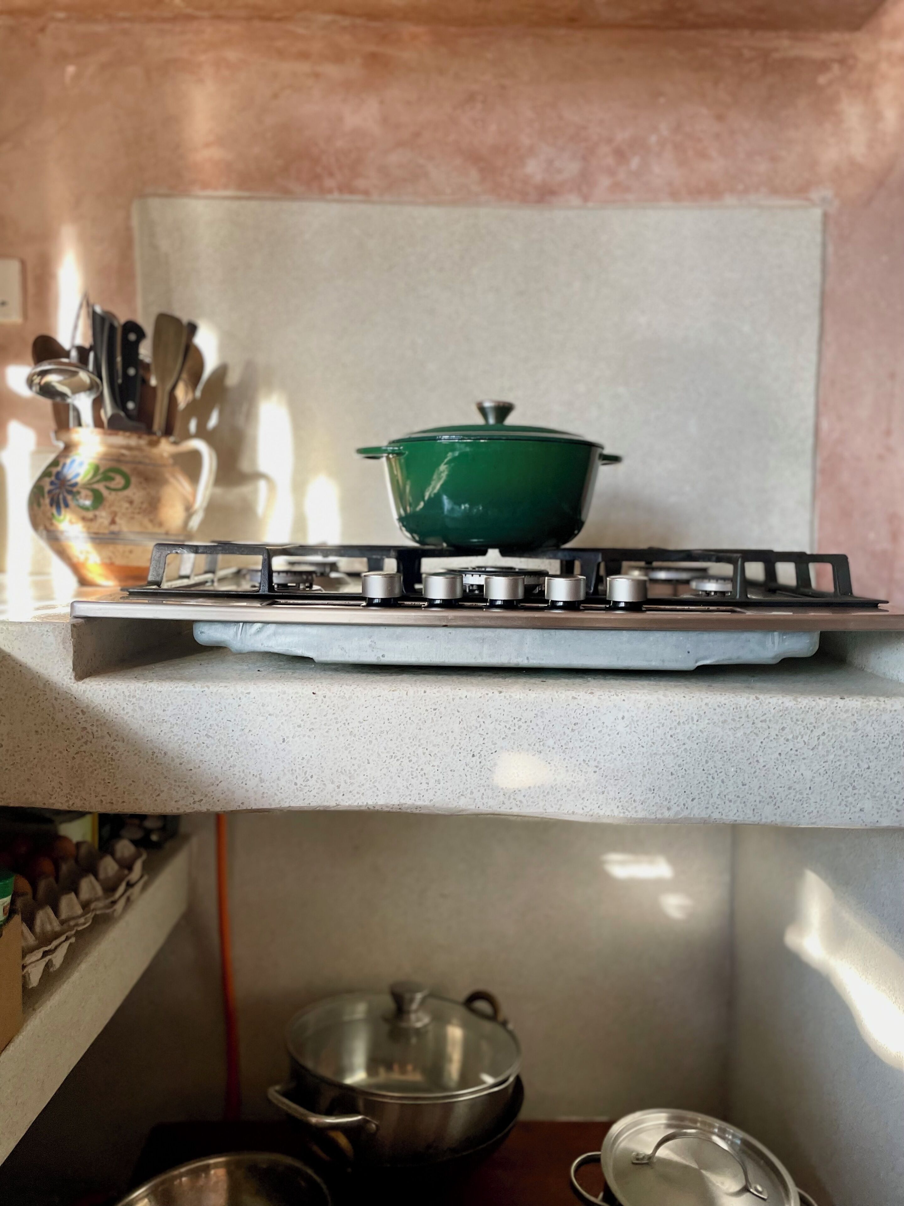 Een keuken met een gasfornuis, een groene pan op het fornuis en diverse keukengerei op de achtergrond.