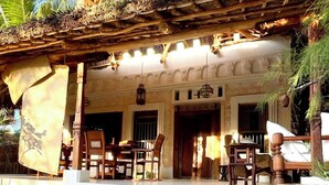 A traditional wooden building with a thatched roof, a dining area with wooden furniture, and a stone pathway leading to the entrance. - Dreamy Beachfront house with pool secluded miles beach Che Shale Malindi Kenya (Che shale Bay, Malindi)