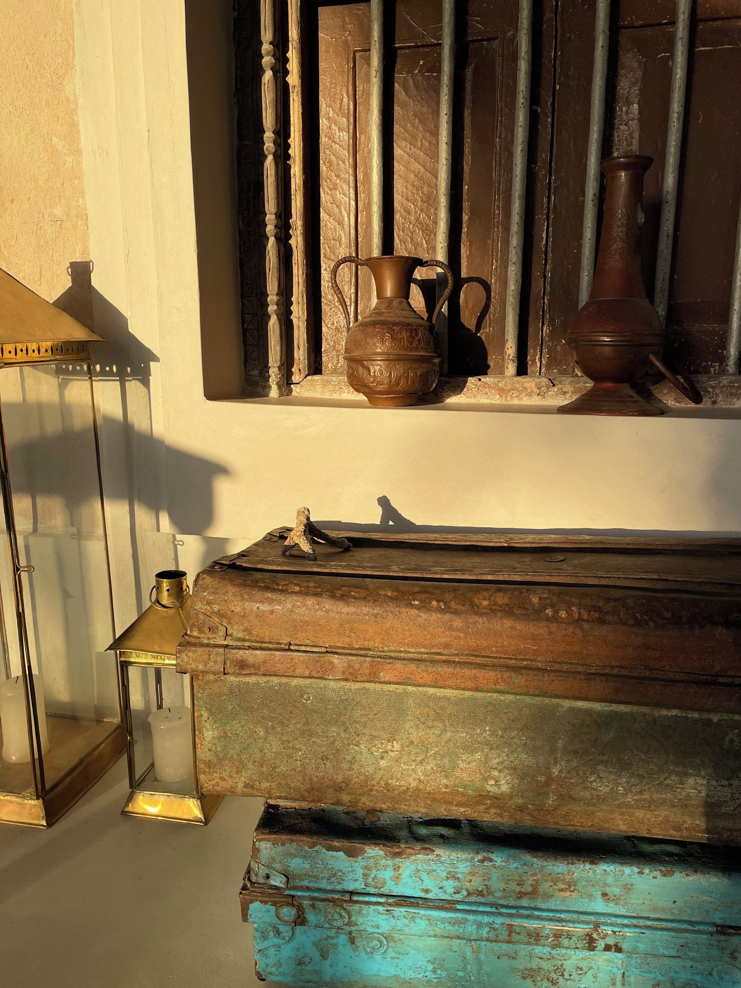 A rustic interior with a wooden chest, a brass lantern, and a ceramic jug on a shelf.
